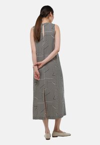 Robe sans manches noire et blanche avec des motifs géométriques, longueur genoux, dotée d'un dos en trou de serrure, et s'associant avec des chaussures plates de couleur claire.