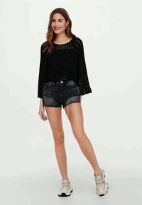 Sort striktop med klokkeærmer, parret med højtsiddende mørke denimshorts. Modellen bærer lyse sneakers.