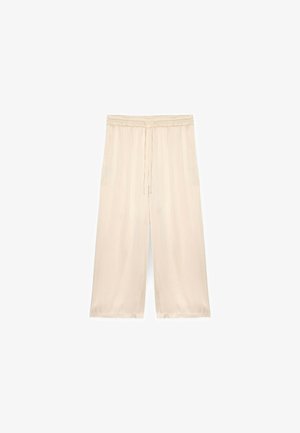 Pantaloni largi, bej deschis, cu talie elastică și șnur. Textură moale și netedă, cu buzunare laterale. Lungime până la jumătatea gambei.