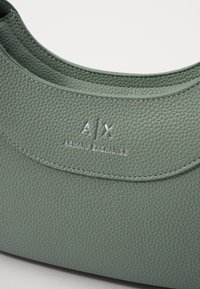 Grønn teksturert lærveske med avrundet design, med preget "A/X" og "Armani Exchange" logo foran.