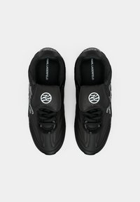 Crne tenisice od sintetičkog materijala s zaobljenim vrhom, podstavljenim jezikom i teksturiranim potplatom. Sadrže logo i kontrastne srebrne detalje.