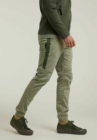 Pantaloni affusolati verde khaki con accenti grigio, caratterizzati da una vestibilità slim e più tasche, abbinati a sneakers verde scuro.