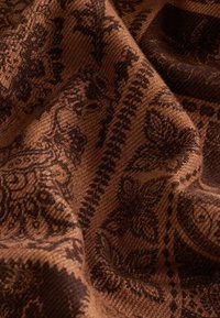 Woven fabric in warm brown tones featuring intricate dark brown floral patterns and geometric accents, with a soft, textured surface.