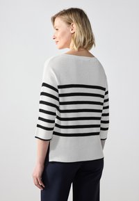 Pull rayé avec des rayures noires et blanches horizontales, texture côtelée, encolure bateau et manches trois-quarts. Porté avec un pantalon foncé.