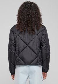 Juodas medvilninis pūkinis švarkas su trumpu, kvadratiniu dizainu. Turtingos deimanto formos raštai ir elastinės rankogaliai. Sklandus, blizgus paviršius.