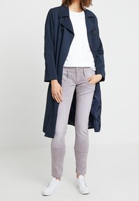 Marinblå långjacka med dubbelknäppta knappar över en vit t-shirt, i kombination med röd- och vitrandiga slim-fit byxor och vita sneakers.