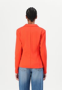 Czerwony dopasowany żakiet z klapami, długimi rękawami i detalem szwu z tyłu, w zestawie z jasnoniebieskimi spodniami szerokimi w nogawkach.