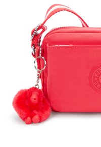 Czerwona torba crossbody z teksturowanej tkaniny, z odpinanym czerwonym futrzanym breloczkiem w kształcie małpki oraz detalem z logo z jednej strony.