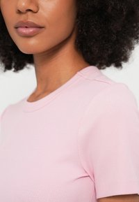 Ροζ φωτεινό ριπ κοντομάνικο μπλουζάκι με στρογγυλή λαιμόκοψη, που παρουσιάζει οριζόντια υφή και λεπτές ραφές.