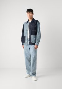 Jeansjakke med en blanding av lyse og mørke blå paneler, med knapper i front, brystlomme og to lommer foran. Kombinert med lyse blå jeans.