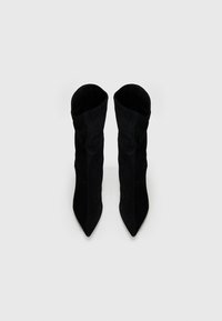 Stivaletti in suede neri alla caviglia con punta appuntita, texture morbida e design sformato, caratterizzati da una silhouette senza cuciture e uno stile minimalista.