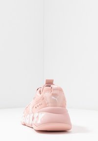 Des chaussures de sport roses avec un dessus en daim texturé, un col rembourré et un marquage blanc prominent sur le côté. Dotées d'une languette de talon en boucle.