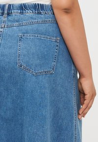 Denimskjørt med elastisk midje som er samlet, lyseblå farge, og en enkelt baklomme med forsterkede sømdetaljer.