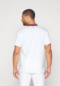 Λευκό πόλο μπλουζάκι κοντομάνικο με σχέδιο ροζ γιακά και λεπτομέρεια λογότυπου στο πίσω μέρος του λαιμού. Λείο ύφασμα με άνετη εφαρμογή.