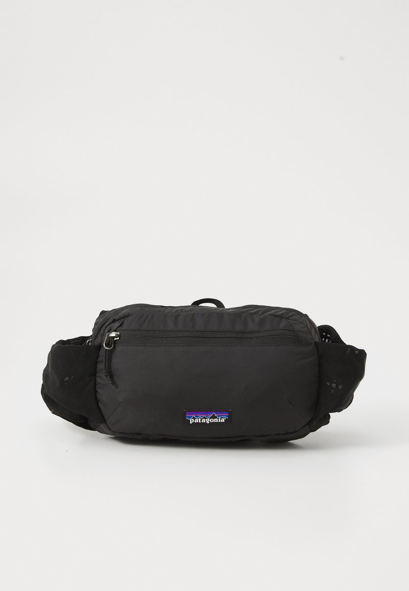 Schwarze Stoff-Wellness-Tasche mit einem Reißverschlussfach, verstellbaren Trägern und einem kleinen Patagonia-Logo-Patch auf der Vorderseite.