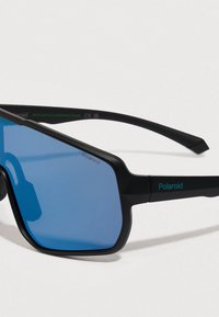Sluneční brýle s černým rámečkem v obdélníkovém tvaru a modrými skly, na kterých je logo Polaroid, umístěné na pozadí bílé barvy.