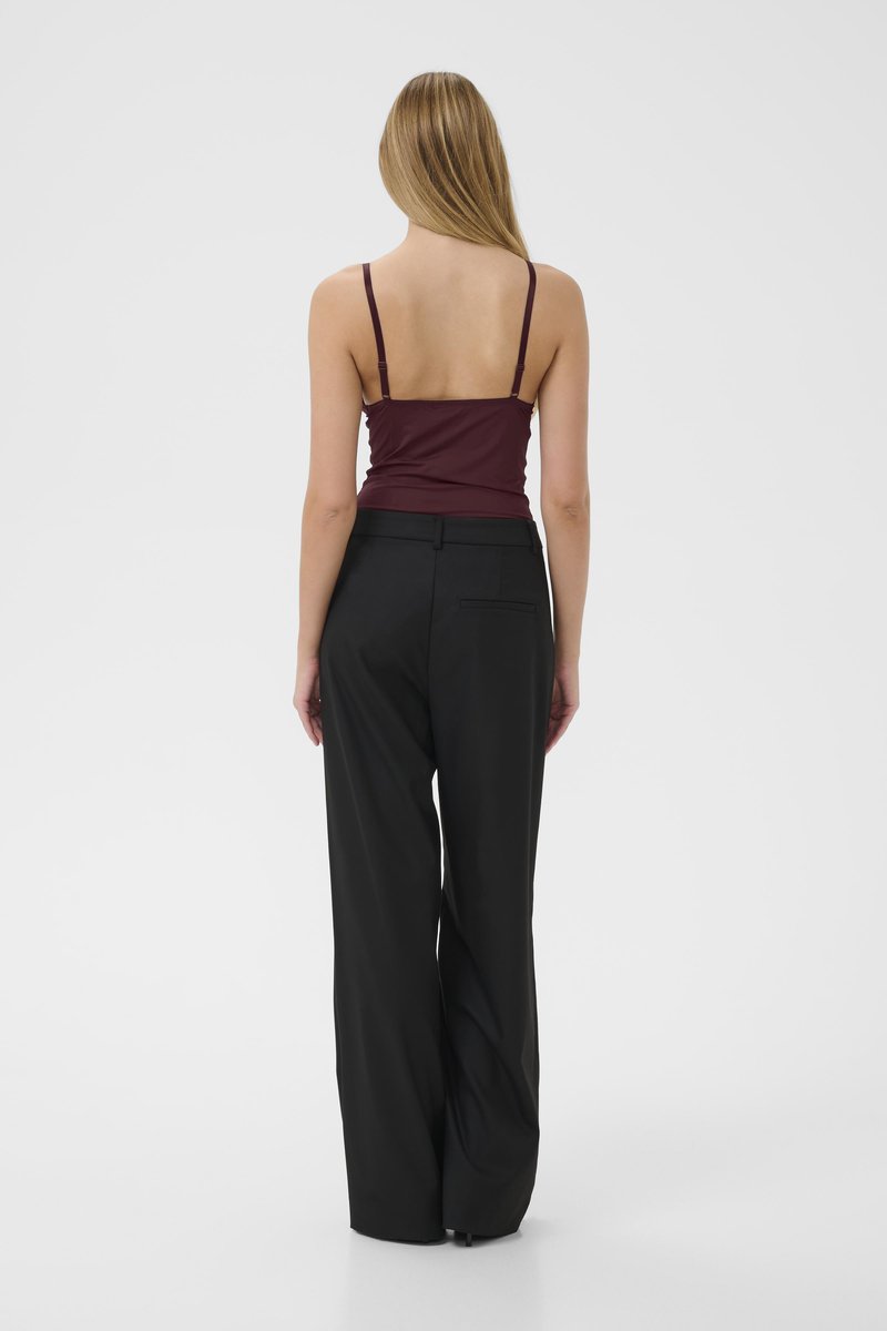 Bordeaux, aansluitende camisole met dunne bandjes, gecombineerd met hoge, brede zwarte broek. Glad textiel, minimale details.