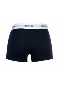 Boxer in cotone blu navy con elastico bianco in vita che presenta il logo "LACOSTE" in nero. Texture liscia e vestibilità standard. Senza cuciture visibili.