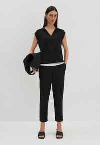 Haut noir à manches courtes et col, superposé à une chemise blanche ; associé à un pantalon noir fuselé et des sandales noires à glissière. Sac tissé noir.