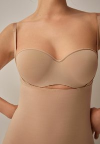 Ljusbeige sömlös bodysuit med justerbara band och ett utskärningsdesign. Tillverkad av mjukt, slätt tyg med matt yta.