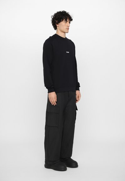 Haut noir à col rond, avec des poignets et un ourlet côtelés. Associé à un pantalon cargo noir ample avec des poches latérales.