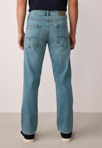 Világoskék farmernadrág egyenes szabással, látható dupla varrással, két hátsó zsebbel és egy egyszerű barna bőr címkével a deréknál.