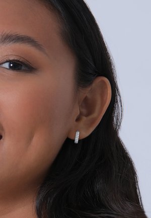 Orecchino a cerchio in argento con superficie texture, decorato con pietre preziose trasparenti, che mostra una finitura lucida e un design cilindrico.