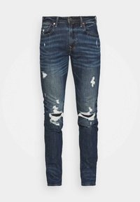 Mörkblå denimjeans med trasiga knädetaljer, slim fit och subtila blekningar. Har standard femfickorsdesign och metallknapp.