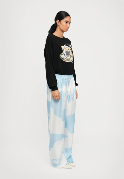 Schwarzer Sweatshirt mit Teetassen-Grafik, kombiniert mit hellblauen, wolkenmusternden weit geschnittenen Hosen. Glattes Material, lässiger Schnitt, elastischer Bund.