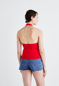 Crvena halter-č top s prilagođenim dizajnom, izrađena od rastezljivog materijala. Uparen s plavim traper gaćama koje imaju rastrgani rub i stražnje džepove.