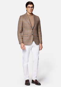 Brązowa marynarka w kratę z niebieskimi akcentami, beżowy golf, białe spodnie i brązowe loafersy. Gładki materiał o dopasowanym kroju.