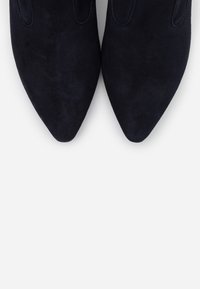 Zapatos de ante azul marino con punta afilada, de textura suave y detalles de costura sutiles, diseñados con una forma elegante y aerodinámica.