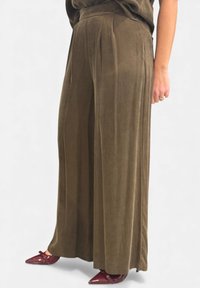 Pantaloni a gamba larga, a vita alta, in tessuto morbido verde oliva con righe verticali e pieghe, abbinati a scarpe color borgogna con punta affilata.