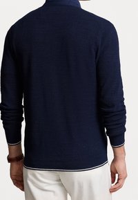 Marinblå stickad tröja med ett strukturerat mönster, lång ärm och vit kant vid muddar och nederkant, med en krage.