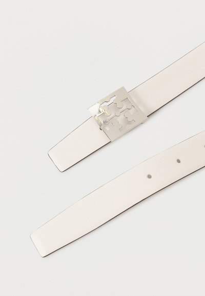 Cinturón de cuero blanco con una hebilla de metal plateado que presenta diseños recortados. El cinturón es suave, tiene un extremo redondeado y múltiples agujeros de ajuste.