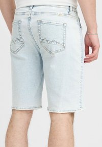 Ljusblå denimshorts med fransade kanter, featuring two back pockets with triangle-shaped stitching. Slät textur, medellång klippning.