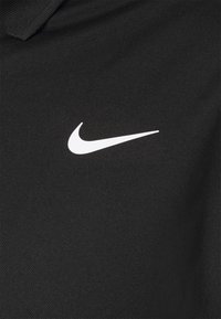 Černé polo tričko vyrobené z texturované tkaniny s bílým logem Nike Swoosh na levé straně hrudi. Standardní design límce.