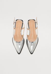 Chaussures slingback argentées à bout pointu avec une finition brillante, semelle extérieure noire et semelle intérieure beige. Dotées d'une fine bride avec boucle réglable.