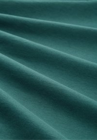 Tessuto turchese con una superficie liscia, caratterizzato da morbide pieghe e un leggero lucido, che mette in evidenza ondulazioni e pieghe nel materiale.