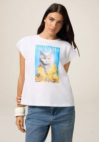Witte t-shirt met korte mouwen, voorzien van een blauwe en gele kattengrafiek met de tekst "DREAMS" erboven. Casual fit met een ronde halslijn.