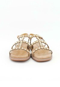 Beiga sandaler med dekorativa cirkulära nitar, öppen tå och tvärgående remmar. Texturerad innersula och platt, något glittrande sula.
