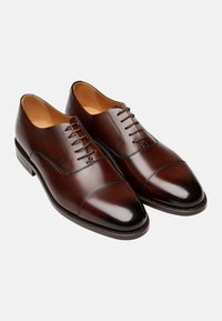 Braune Lederschuhe mit glatter Oberfläche, mit Kappenzehen-Design und geschlossenen Schnürsenkeln. Verfügt über dezente Nähte und eine abgerundete Schuhspitze.