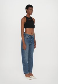 Débardeur noir cropped avec un détail découpé, associé à un jean taille haute bleu clair et des chaussures blanches à bout pointu.