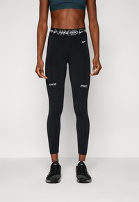 Leggings neri realizzati in un tessuto elasticizzato con una vestibilità aderente. Presentano una cintura ampia con il marchio "NIKE PRO" e dettagli in bianco del logo.