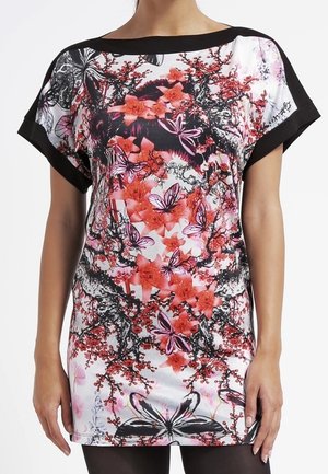 Robe courte à imprimé floral et papillons avec bordure noire aux manches et à l'encolure, portée par une personne debout, les bras détendus le long du corps.