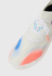 Weiße Fußballschuhe mit einer strukturierten Oberfläche, die blaue und korallenfarbene Farbverläufe aufweist, weißen Schnürsenkeln und einem sockenähnlichen Kragen design.