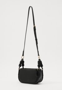 Black leather crossbody bag with a rounded shape, knotted fabric straps, and gold-tone hardware accents. Smooth texture, minimalist design.
