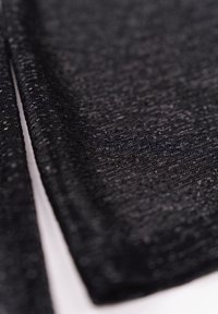 Schwarzer strukturierter Stoff mit einem leichten Glanz, der ein gewebtes Muster aufweist, das Tiefe verleiht. Glatte Oberfläche, an den Kanten gefaltet.