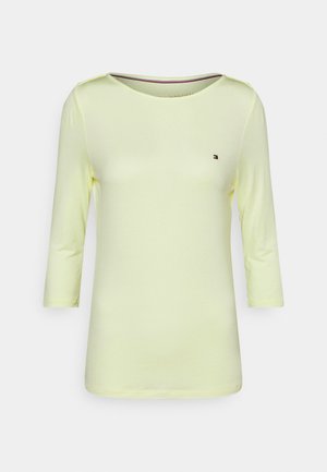 Chemise jaune clair à manches longues avec un col rond et un petit logo Tommy Hilfiger sur la poitrine gauche.