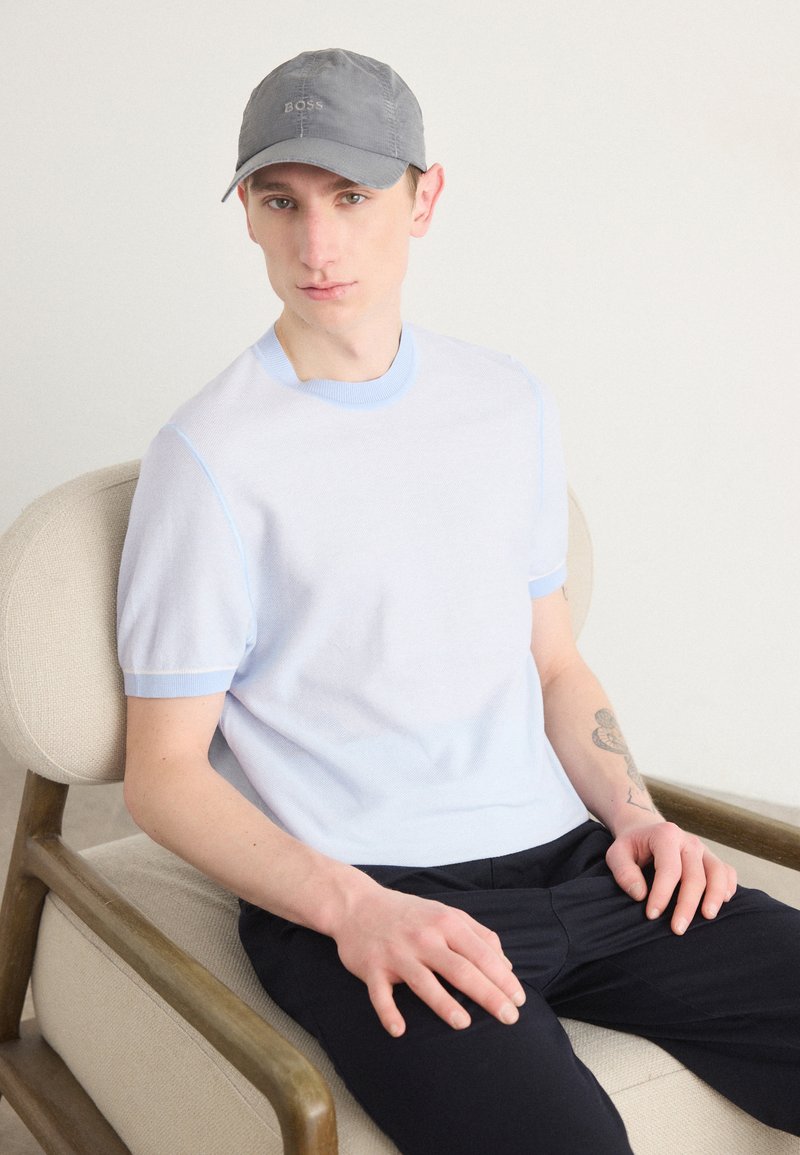 Maglietta in maglia blu chiaro con maniche corte e scollatura rotonda, con un bordo blu a contrasto; cappellino grigio con logo "BOSS".